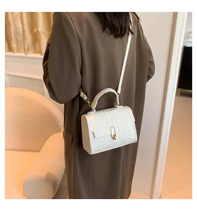 Detailed view of white crocodile pattern crossbody bag with golden round buckle and handle