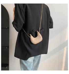 Detail of beige crescent bag with crocodile pattern texture and gold chain strap