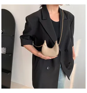 Detail of mini crescent bag with animal texture and gold chain on black blazer
