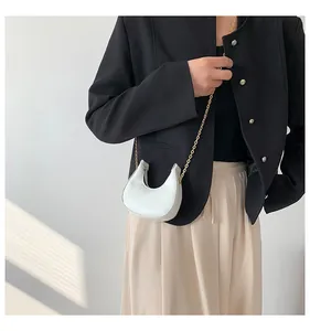 Detail of white crescent crossbody bag with faux crocodile skin texture and gold chain strap