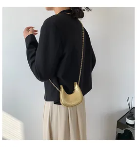 Golden crescent crossbody bag with crocodile texture and metal chain on a model