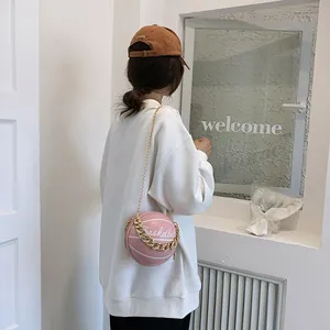 Pink basketball shaped crossbody bag with gold chain strap worn by a model in a white hoodie
