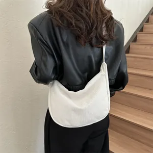 Sac à bandoulière demi-lune en velours côtelé blanc porté par un mannequin chic