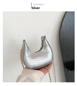 Detail of silver crescent bag with metallic scale texture and gold chain strap held by hand