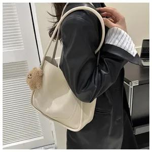 Sac fourre-tout chic en similicuir crème avec breloque ours brun porté par un mannequin