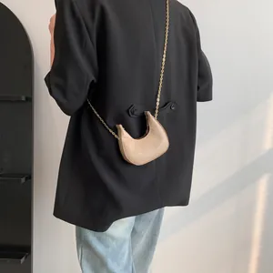 Beige crescent bag with crocodile pattern and gold chain strap shown on a model