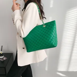 Fashionable green quilted tote bag with golden chain strap worn with a white blazer