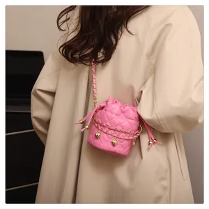 Detail of pink quilted bucket bag featuring gold chains and heart charms on a trench coat