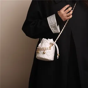 White quilted bucket bag with golden chain and heart charms shown on a model