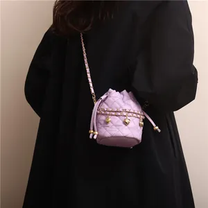 Quilted lavender bucket bag with golden chain and heart charms on a black coat