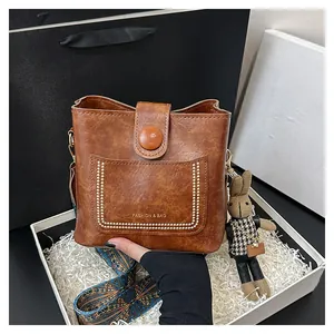 Close-up of brown bucket bag with wide printed strap and cute bunny charm in gift box