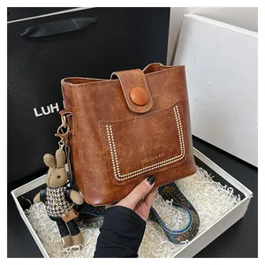 Detail of a brown bucket bag featuring a woven strap and cute bunny pendant charm