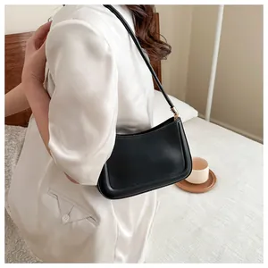 Sac baguette minimaliste en cuir noir porté à l'épaule avec des détails dorés chic