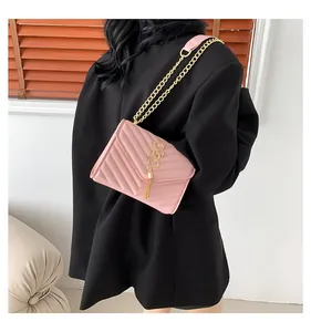 Close-up of pink quilted crossbody bag with golden logo and fringe detail on black suit