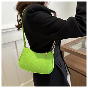 Detail of neon green crossbody bag with V-quilt texture and gold chain strap on model
