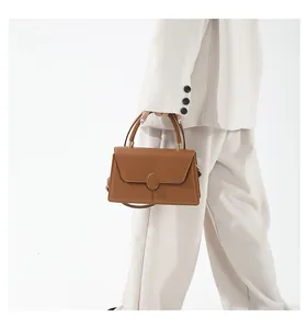 Detail der karamellbraunen Handtasche mit Metallschnalle und Griff auf weißem Outfit