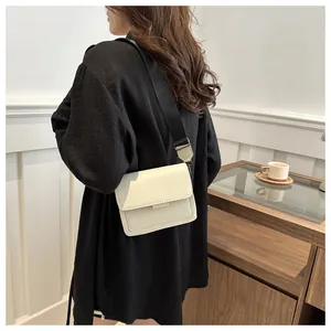 Minimalist beige crossbody bag with black wide shoulder strap and leather finish details