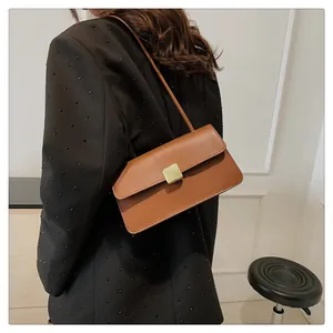 Détail d'un sac bandoulière en cuir marron avec boucle dorée porté sur un blazer noir