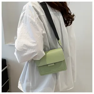 Detail view of light green crossbody bag with a wide black woven strap on a model