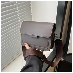 Detail of dark brown rectangular flap shoulder bag with wide strap in hand-held view