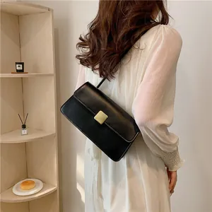 Sac bandoulière rétro noir avec boucle dorée porté par un mannequin dans un cadre cosy