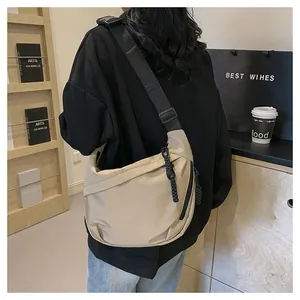 Close-up of beige nylon crescent tote bag with wide adjustable shoulder strap on a model
