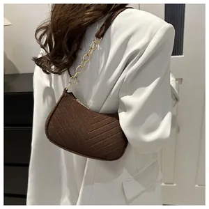 Detail of dark brown V-quilted crossbody bag with gold chain strap on white blazer