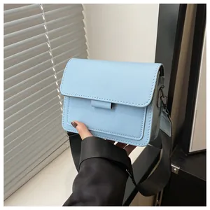 Detail view of light blue crossbody bag with wide black nylon strap and metallic buckles