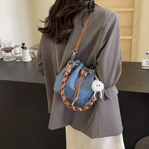 Blue denim bucket bag with brown leather strap and plush charm worn on shoulder