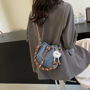 Blue denim bucket bag with brown woven handle and plush charm on a female model