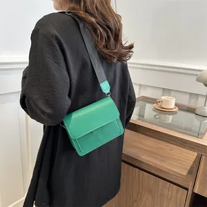 Minimalist green square crossbody bag with wide black strap shown on a model