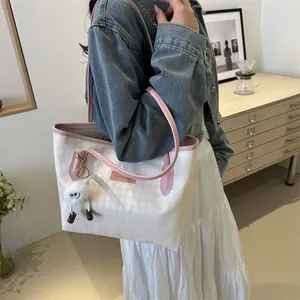 Borsa tote bianca pied de poule con rifiniture rosa e ciondolo indossata a spalla