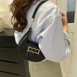 Sac sous le bras chic en crocodile noir avec boucle dorée porté par un mannequin