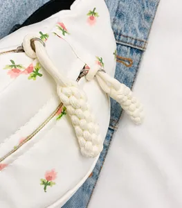 Close-up of white floral waist bag with silver zipper and woven rope detail