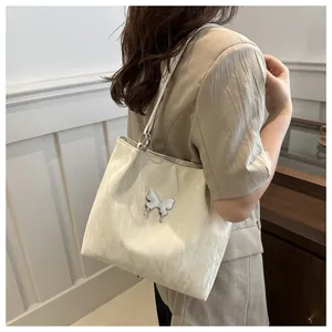 Détail d'un sac cabas blanc crème avec ornement papillon argenté et texture plissée