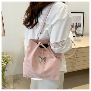 Détail d'un sac cabas rose clair avec logo papillon en métal argenté et fines lanières