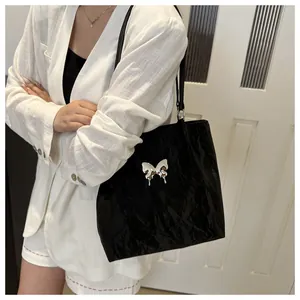 Détail du sac cabas plissé noir avec accessoire papillon argenté sur texture en cuir