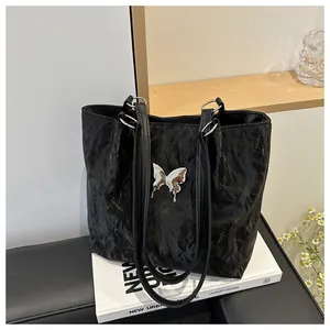 Détail du cabas noir avec texture froissée et pendentif papillon argenté sur fond en bois