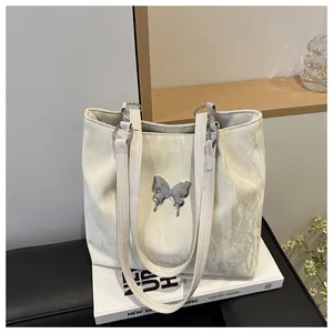 Détail du sac cabas blanc avec texture plissée et boucle papillon argentée brillante