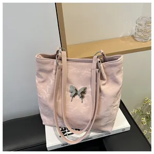 Détail du cabas rose clair avec texture ondulée et ornement papillon en métal argenté