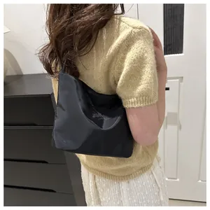 Detail of black satin bucket bag with subtle embossed logo held by model in knitwear