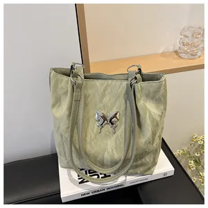 Détail du sac cabas plissé vert clair orné d'un papillon métallique argenté élégant
