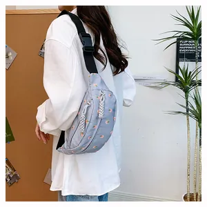 Detail of light blue waist bag showing pink floral embroidery and woven rope zipper pull