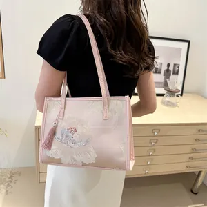 Pink tote bag with floral embroidery and tassel charm shown on woman’s shoulder
