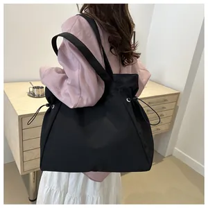 Detail of black tote bag with side drawstrings and wide shoulder straps in a home setting
