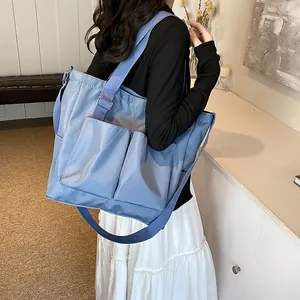 Blue nylon tote bag with front pockets and adjustable strap shown on a model