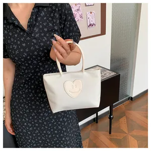 Detailed shot of cream-white mini handbag with heart smiley patch and GUBERMUTHVANDIAM logo