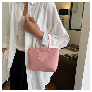 Close-up of pink tote bag featuring a heart-shaped smiley face embroidery and handle detail