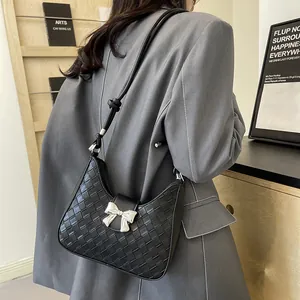Minimalist black woven shoulder bag with silver bow accent shown on model in grey blazer