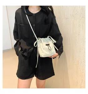 Close-up of beige drawstring bucket bag worn by model on a black minimalist outfit